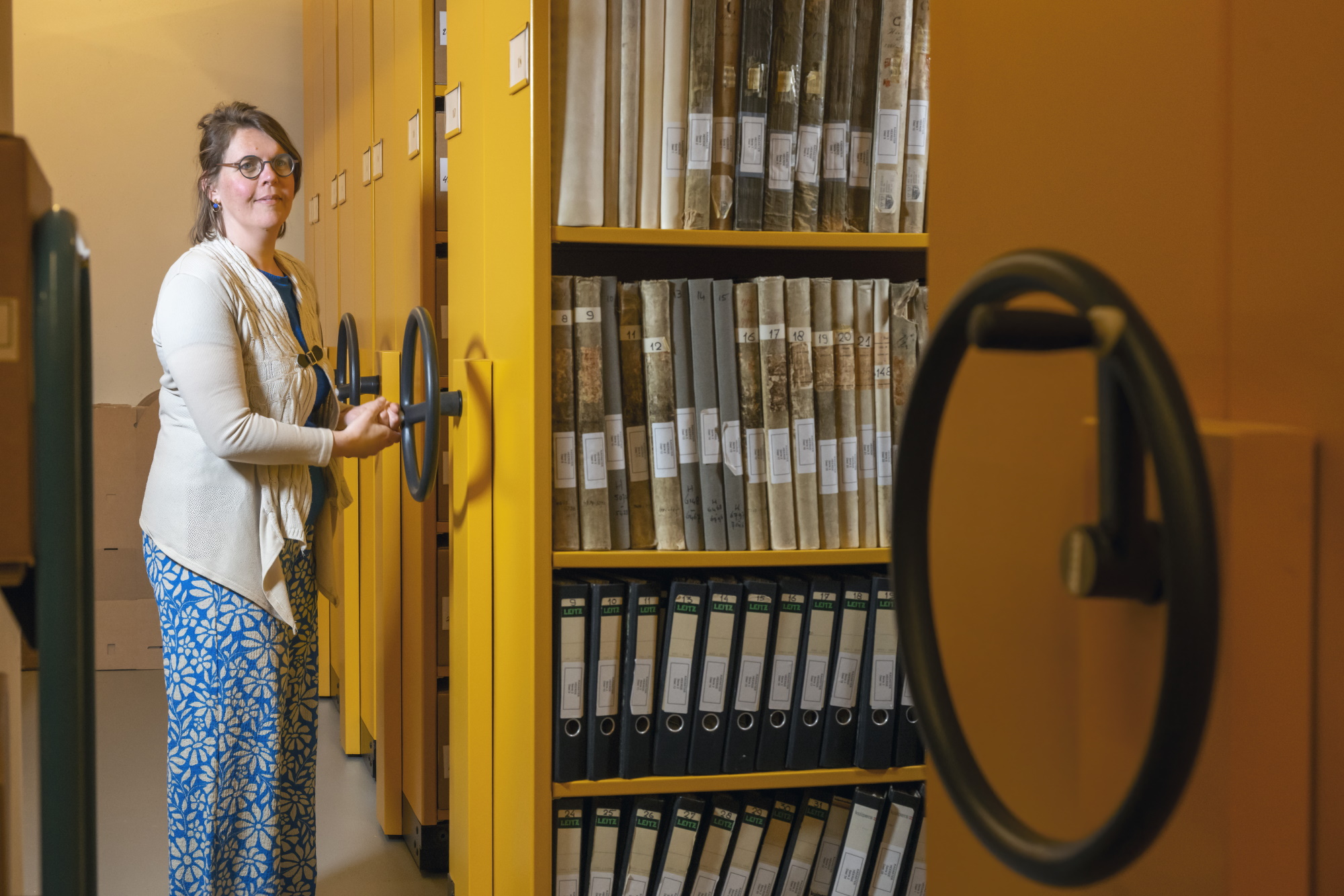 Een vrouw draaiend aan een wiel van een gele stellingkast.