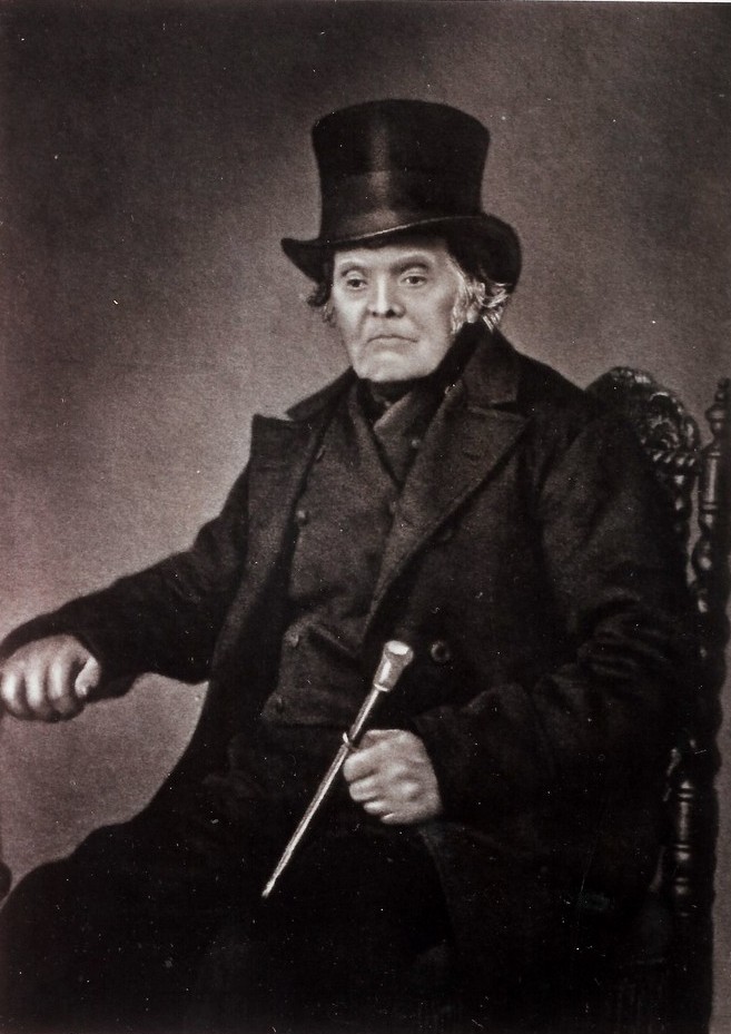 Foto van Frans Gunnink (1788 - 1878). Wagenmaker te Wezep en vanaf 1827 woonachtig in Kampen. Hij is afgebeeld in zwarte jas met een stok in de linkerhand. Hij heeft een hoge hoed op en bakkebaarden.