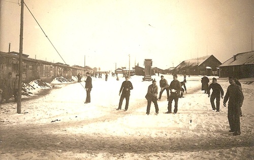 6900 Fotocollectie Interneringskamp Oldebroek - Sneeuw gooiende geïnterneerde Belgen in Kamp Oldebroek Een foto in sepia. Met op de voorgrond een aantal mannen in uniform. Rechts op de achtergond staat twee gebouwen. Links staan ook gebouwen.