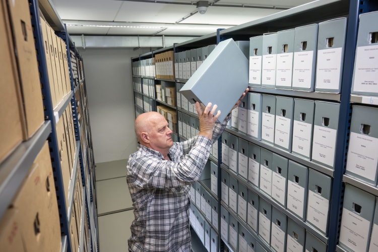Een man staat in een archiefdepot en zet een blauwe archiefdoos terug in de stelling
