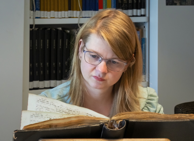 Een vrouw met een bril kijkt naar een archiefstuk, waar ze onderzoek naar doet in onze studiezaal.