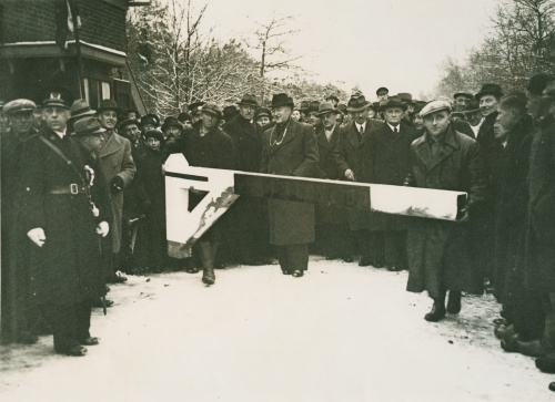 Zwart wit foto met van links naar rechts een groep mensen achter een slagboom.