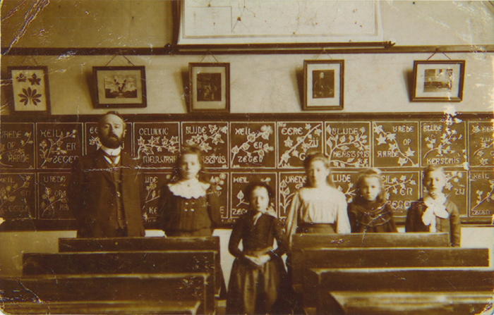 Een foto in een klas met aan de linkerkant een man en daarnaast vier meisjes en een jongetje. Op de voorgrond staan schoolbanken.